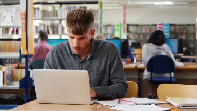 Masculino-estudiante-trabajando-en-ordenador-portátil-en-la-biblioteca-de-la-Universidad