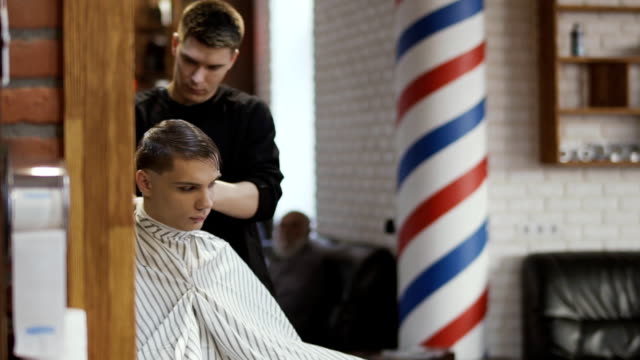 Professionelle-Friseur-macht-Frisur-mit-elektrischen-Rasierapparat-mit-einem-jungen-Mann