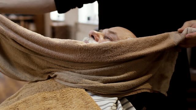 Barber-covers-face-of-mature-man-with-a-hot-towel-before-shaving-the-beard