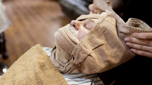 Barber-covers-face-of-old-man-with-hot-towel-before-shaving