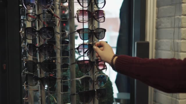 Woman-is-rotating-a-stand-with-trendy-sunglasses-in-a-shop,-view-of-hand