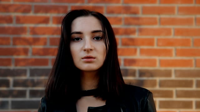 Portrait-of-a-young-serious-sexy-woman-against-a-brick-wall.-Slow-motion-shot.