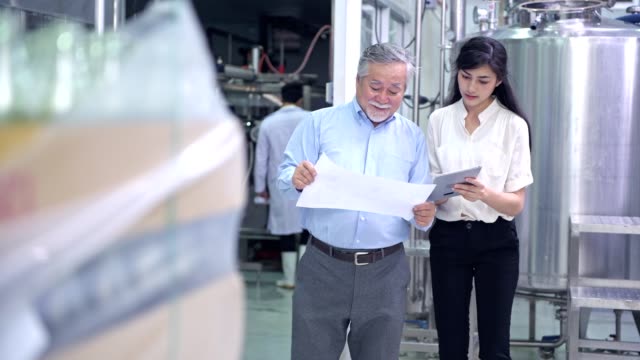 Factory-owner-inspecting-his-production-line.-Asian-senior-man-with-beautiful-asian-female-personal-assistant-talking-inside-factory.