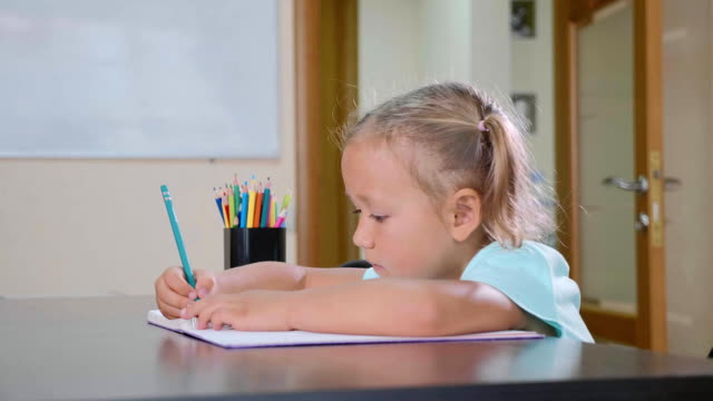 Little-cute-girl-sits-in-classroom-and-writing-in-exercise-book