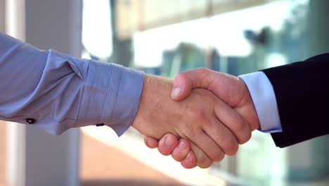 Close-up-of-two-successful-businessmen-greeting-each-other-in-urban-environment.-Young-colleagues-meeting-and-shaking-hands-near-office-building.-Handshake-of-business-partners-outdoor.-Side-view