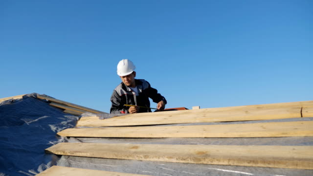 Adulto-profesional-constructor-de-longitud-medición-casco-de-madera-de-la-madera-en-sitio-bajo-el-cielo-azul
