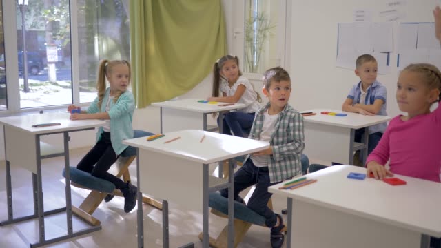 los-niños-en-la-escuela,-los-niños-y-niñas-se-sientan-en-escritorios-y-elevar-las-manos-durante-la-lección-en-clase-en-la-escuela