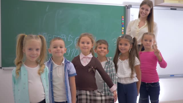 Gruppe-von-Grundschulkindern-mit-jungen-Erzieher-Lächeln-und-schauen-Sie-sich-die-Kamera-auf-Grund-von-blackboard