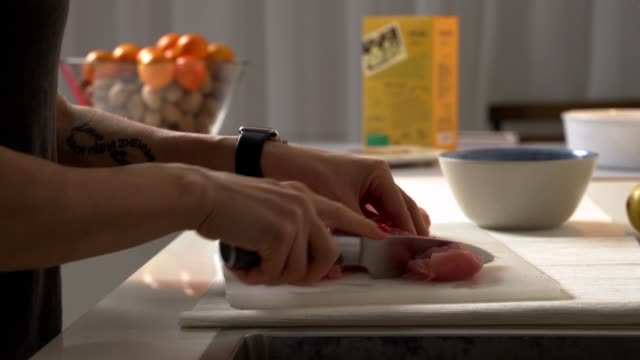 Close-up-woman-cuts-chicken-with-a-knife-on-a-Board.-Female-hands-chef-cutting-raw-chicken-meat-breast.