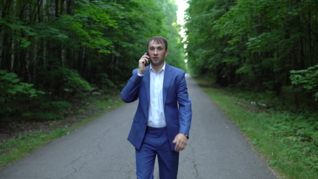 junger-Geschäftsmann-in-einem-blauen-Anzug-zu-Fuß-entlang-der-Straße-und-am-Telefon-sprechen