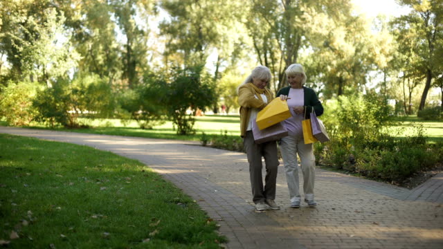 Elder-women-walking-in-park,-showing-and-boasting-purchases-they-buy-in-shop