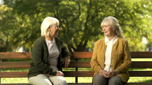 Dos-mujeres-mayores-alegres-disfrutando-de-la-compañía-de-personas-transeúntes-en-el-parque,-mayor