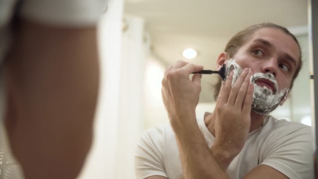 Man-Shaving-Beard-With-Razor-In-Bathroom