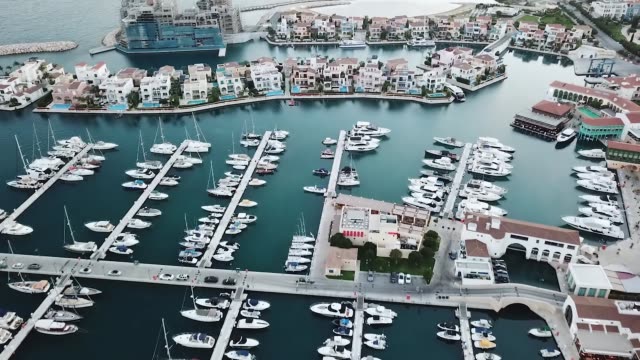 die-Drohne-fliegt-über-die-Marina-in-Limassol,-weiße-Yachten-und-Häuser-auf-dem-Hintergrund-von-türkisfarbenem-Wasser
