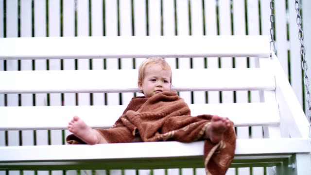 a-little-one-year-old-girl,-wrapped-in-a-towel,-with-a-dirty-face,-lonely-sitting-on-a-swing-in-the-garden,-in-the-summer.-She-has-a-sad-look.-She-wants-to-sleep