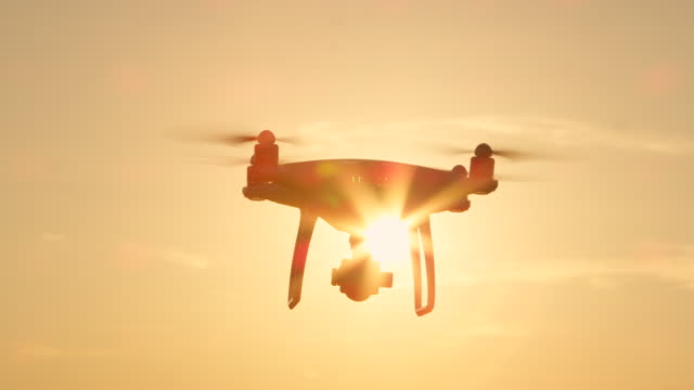 CLOSE-UP-LENS-FLARE-SILHOUETTE:-Dreharbeiten-Drohne-mit-Kamera-überfliegt-der-aufgehenden-Sonne