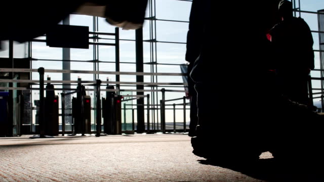 Silhouettes-of-people-walking-by-gates-at-airport-terminal,-flight,-bottom-view