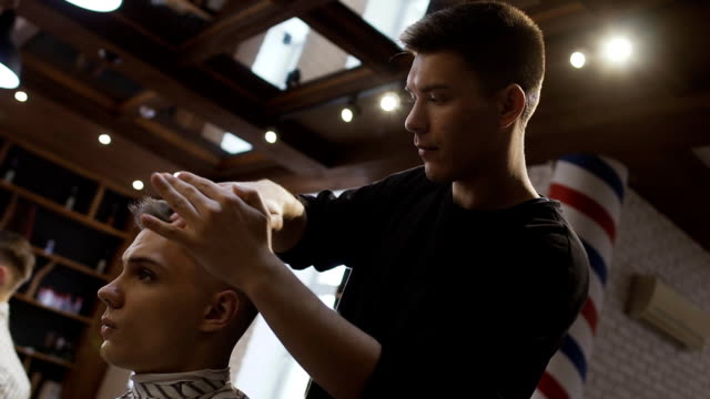 Professional-stylist-makes-hair-styling-for-young-man-in-barbershop