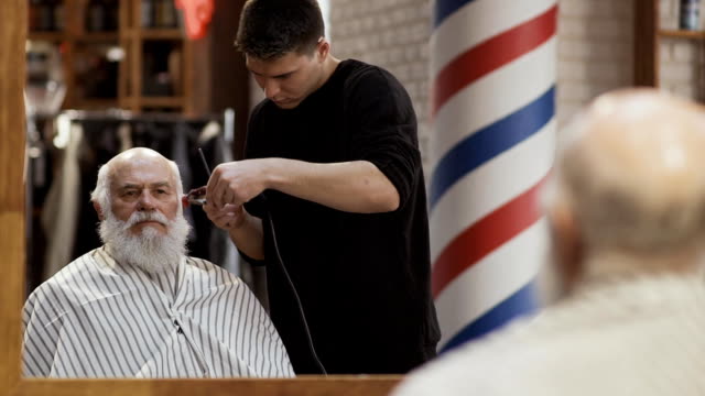 Hairstylist-cuts-gray-hair-of-mature-man-in-barbershop