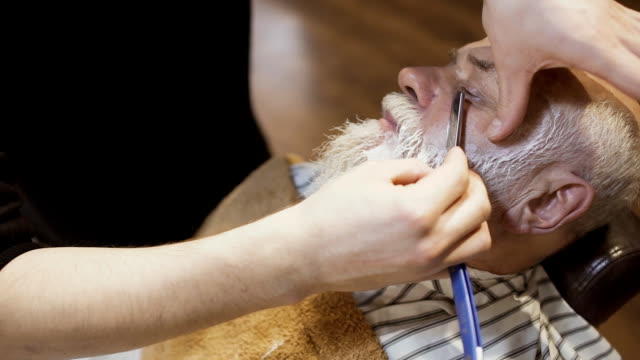 Barber-shaves-face-of-elderly-man-with-blade-and-cream