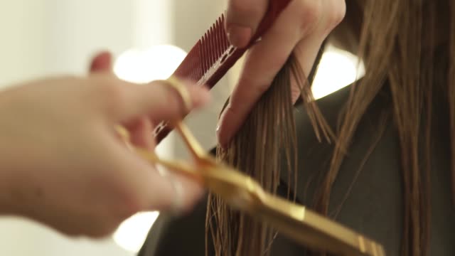 Weibliche-Hand-Friseur-lange-Haare-zu-kämmen-und-Schneiden-mit-Friseurscheren.-Frau-Friseur-mit-professionellen-Schere-im-Beauty-Salon-hautnah