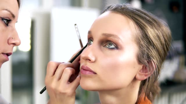 Make-up-studio.-Professional-make-up-artist-doing-make-up-for-a-beautiful-caucasian-model.-Applying-some-eyeshadows-using-a-brush.-Eyes-make-up