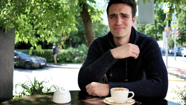 Portrait-of-Crying-Sad-Young-Man-Sitting-in-Cafe-Terrace