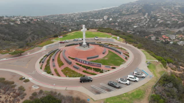 MT.-Soledad-Drone-volando-lentamente-sobre-el-monumento-de-la-Cruz-en-San-Diego,-California-con-coches,-árboles,-hierba-y-a-la-vista-de-la-costa
