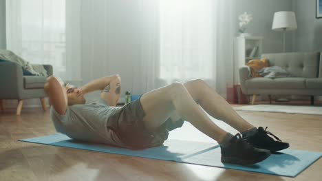 Strong-Athletic-Fit-Man-in-T-shirt-and-Shorts-is-Doing-Abdominal-Crunch-Exercises-at-Home-in-His-Spacious-and-Bright-Living-Room-with-Minimalistic-Interior.