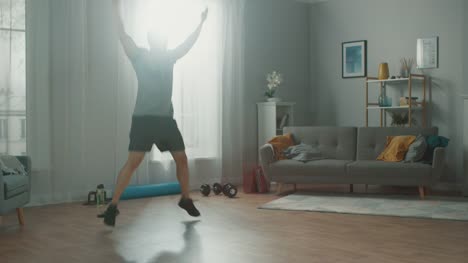 Strong-Athletic-Fit-Man-in-T-shirt-and-Shorts-is-Doing-Jumping-Jack-Exercises-at-Home-in-His-Spacious-and-Bright-Apartment-with-Minimalistic-Interior.