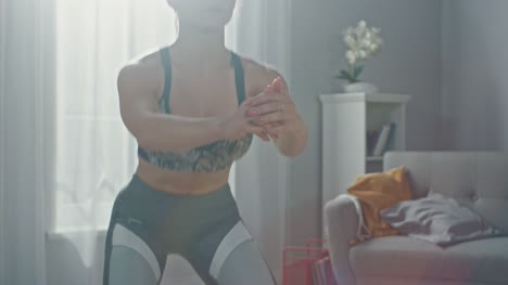 Close-Up-of-a-Fit-Beautiful-Busty-Girl-in-an-Athletic-Top-Doing-Squat-Exercises-in-Her-Bright-and-Spacious-Living-Room-with-Minimalistic-Interior.