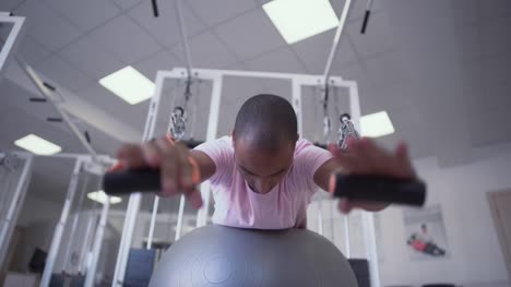 African-American-Kerl-Übung-auf-dem-Simulator-auf-Therapie-Ball-liegend.-Pädiatrische-Physiotherapie