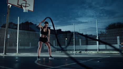Schöne-energetische-Fitness-Girl-Übungen-mit-Battle-Ropes.-Sie-ist-ein-Training-in-einem-eingezäunten-Basketballfeld-im-freien-tun.-Abend-Footage-nach-Regen-in-einer-Wohngegend.