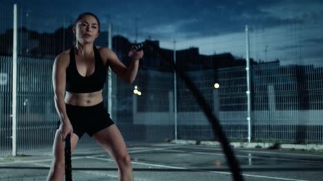Beautiful-Energetic-Fitness-Girl-Doing-Exercises-with-Battle-Ropes.-She-is-Doing-a-Workout-in-a-Fenced-Outdoor-Basketball-Court.-Evening-Footage-After-Rain-in-a-Residential-Neighborhood-Area.