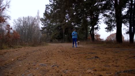 Deportiva-mujer-correr-con-perro-en-el-bosque-del-otoño