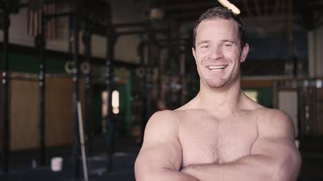 A-fit-young-man-at-a-small-gym-drinks-out-of-a-water-bottle-and-then-smiles-at-the-camera