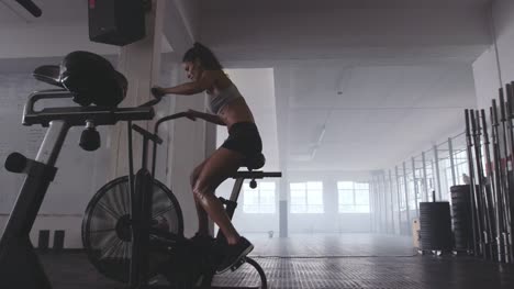 Ajuste-mujer-joven-usando-la-bicicleta-de-ejercicio-en-el-gimnasio
