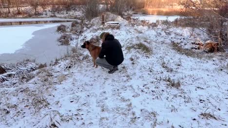 Mann-trainiert-den-Hund-in-der-Nähe-von-Teich-im-Winter