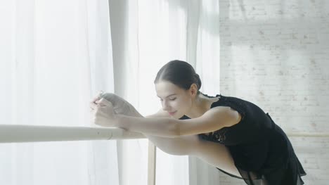 Close-up-of-a-Young-and-Beautiful-Ballerina-Doing-Leg-Stretching-at-the-Barre.-Shot-on-a-Sunny-Morning-in-a-Spacious-and-Light-Studio.-In-Slow-Motion.