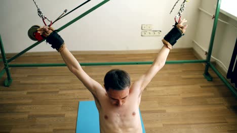 Junger-Mann-tun-Exircise-auf-Kasernierung,-Fitnessgeräte-und-ziehen-Sie-seine-Arme-und-Beine-mit-Seilen