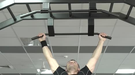 Athlete-muscular-fitness-male-model-pulling-up-on-horizontal-bar-in-a-gym