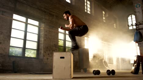 Athletic-Shirtless-Fit-Man-Energetically-Box-Jumps-in-Hardcore-Gym-doing-Part-of-Cross-Fitness-Training-Program.-Man-is-Sweaty-from-Intense-Workout/-Exercise,-Gym-is-in-Industrial-Factory-Location.