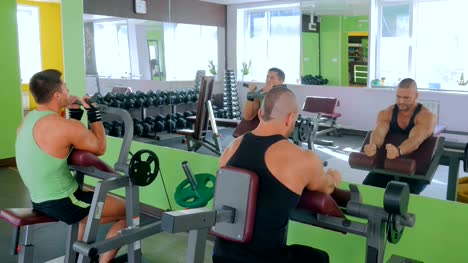 Zwei-sportliche-junge-Männer-arbeiten-auf-Fitness-Trainingsgeräten-im-Fitnessstudio