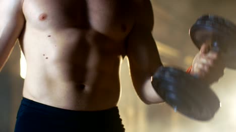 Primer-plano-del-torso-de-un-hombre-sin-camisa-hace-rizos-de-bíceps-con-ejercicios-de-pesas,-como-parte-de-su-entrenamiento-de-gimnasio-de-musculación.