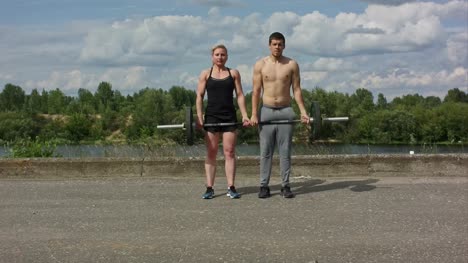 Young-happy-sports-couple-working-out-with-barbell-together