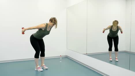 Junge-Frau-mit-Hanteln-macht-Übungen-für-Arme-vor-Spiegel