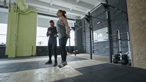 Frau-tut,-springen-Seil-Übung-mit-Trainer-im-Fitness-Studio