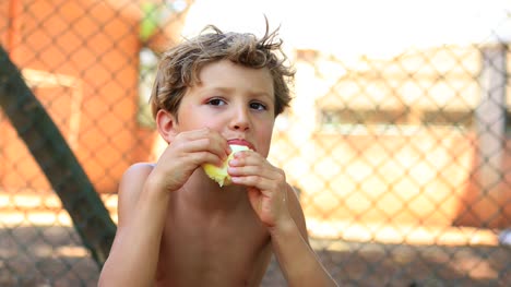 Cándido-retrato-de-niño-guapo,-comer-una-naranja-fuera-en-4K
