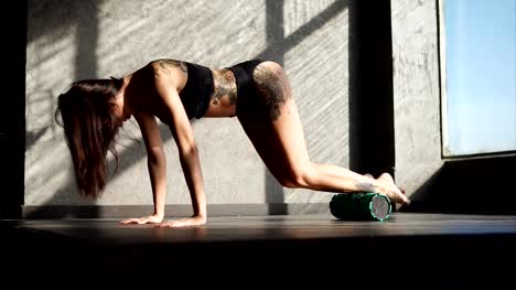 woman-with-a-tattoo-uses-a-roller-for-warming-up-muscles-in-a-fitness-club