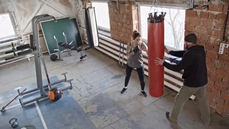 Weiblichen-Boxer-schlagen-Boxsack-beim-Training-mit-Trainer